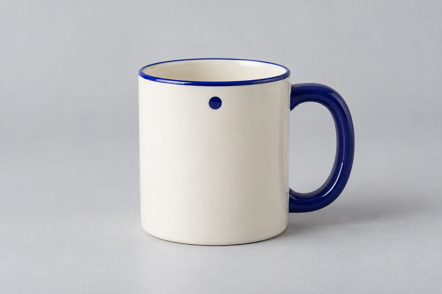 An ivory cylindrical mug with a cobalt-blue handle on the right, a thin blue rim, and a small blue dot on the front.