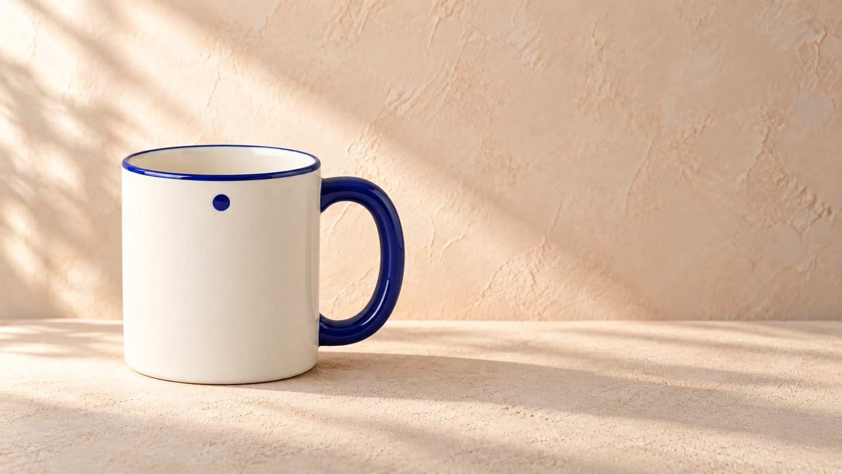 The ivory mug stands on the left against a warm plaster background. Its blue handle, rim, and dot are visible; the right half contains textured wall and a light gradient, without props or text.